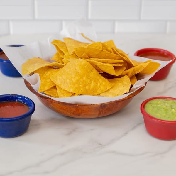 A wooden bowl of tortilla chips with small red and blue bowls of salsa and guacamole.