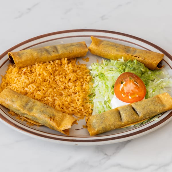Four taquitos with rice, shredded lettuce, guacamole, sour cream, and a tomato slice on a plate.