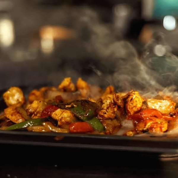 Sizzling chicken fajitas with colorful peppers and onions on a hot plate, emitting steam.