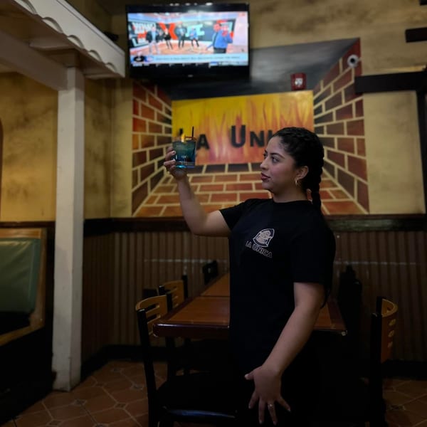 A La Unica employee holds up a blue drink in the restaurant dining area.