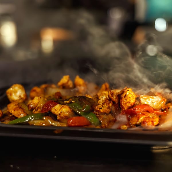 Sizzling chicken fajitas with colorful peppers and onions on a hot skillet, steam rising.