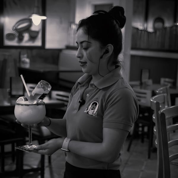 A La Unica server pouring a small bottle into a large margarita with a lime.