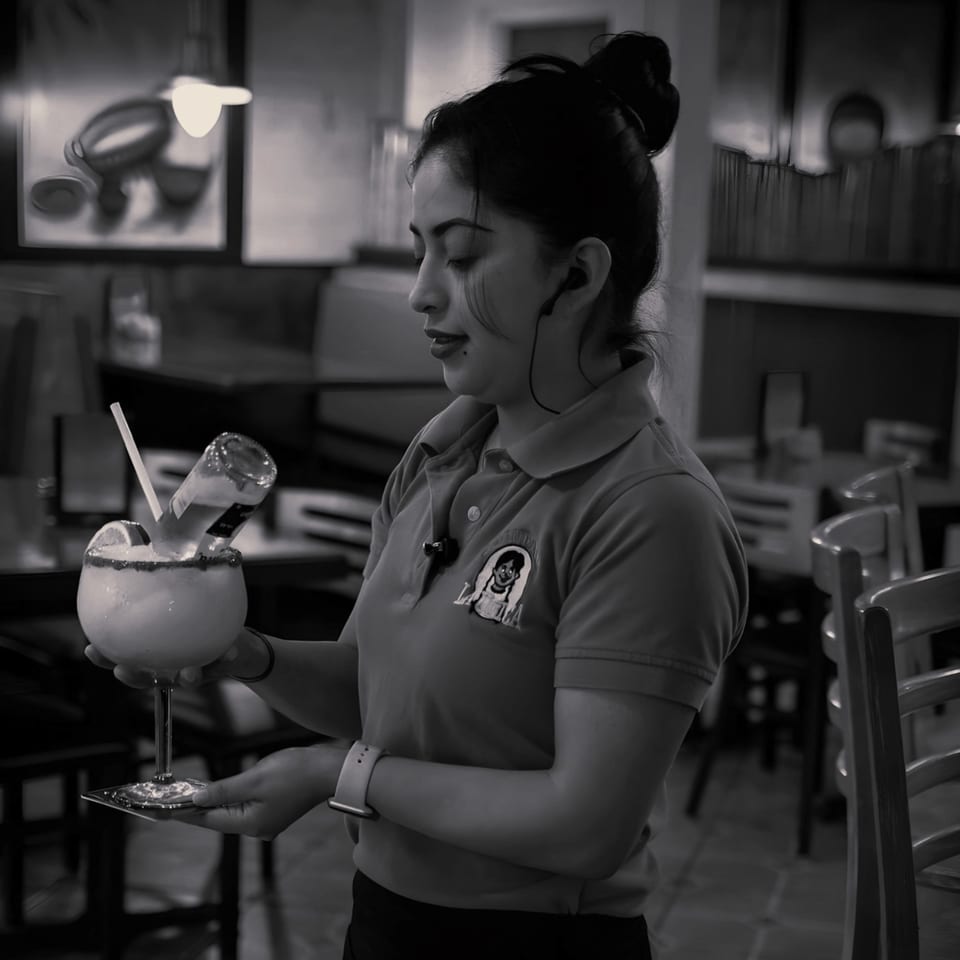 A La Unica server pouring a small bottle into a large margarita with a lime.