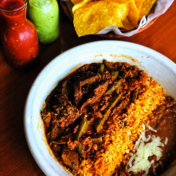 A bowl of La Unica's Mexican food with meat, rice, beans, and cheese, with salsa and chips.