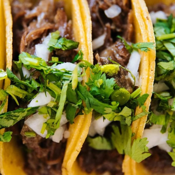 Close-up of three La Unica Mexican Restaurant tacos filled with meat, onions, and cilantro.