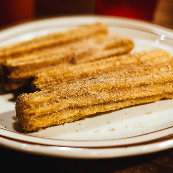 Three golden-brown churros, generously coated in sugar, rest on a white plate at La Unica Mexican Restaurant.