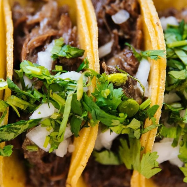 Close-up of three La Unica Mexican Restaurant tacos filled with meat, onions, and cilantro.