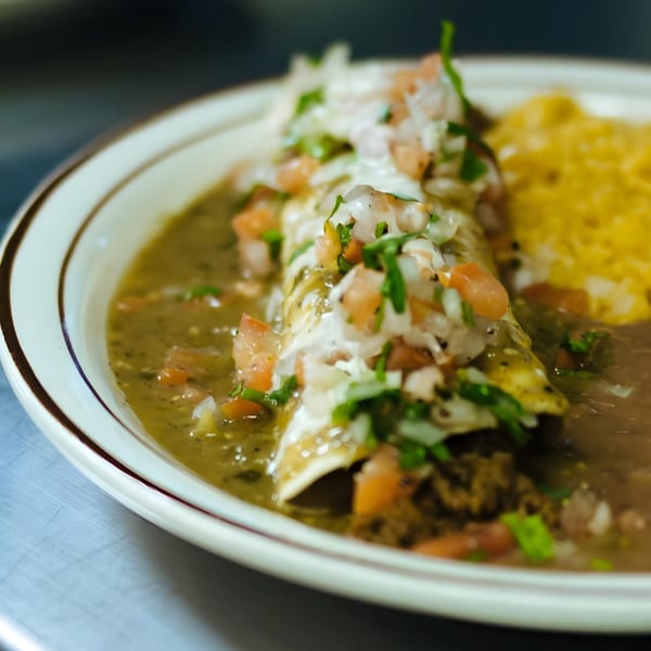 A La Unica Mexican Restaurant enchilada covered in green sauce, pico de gallo, and sour cream.