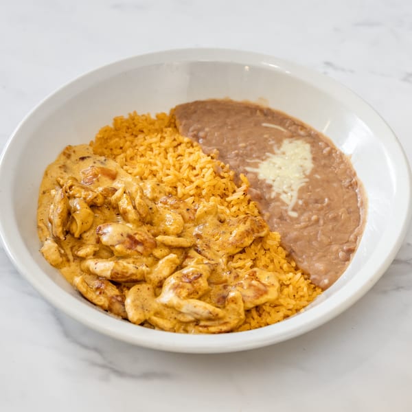 Creamy chicken with yellow rice and refried beans topped with cheese in a white bowl.
