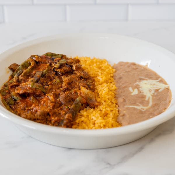 La Unica's carne guisada with rice and refried beans, topped with cheese, in a white bowl.