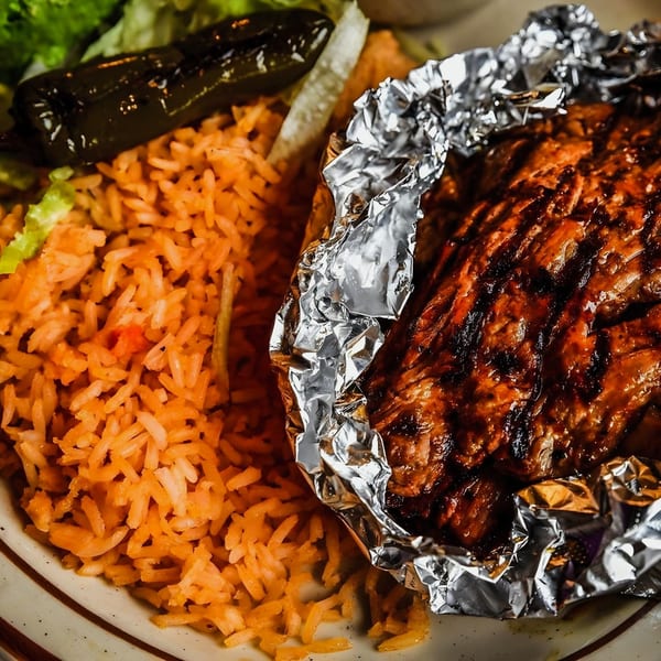Grilled meat in foil, Mexican rice, and a charred jalapeño on a plate.