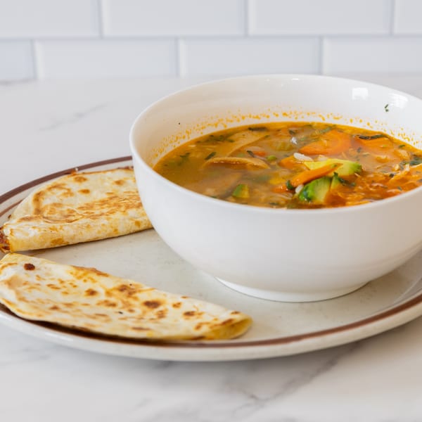 A white bowl of La Unica Mexican Restaurant's vegetable soup with two quesadillas on a plate.