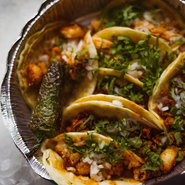 Several La Unica Mexican Restaurant tacos with meat, onions, and cilantro, served in a foil container.