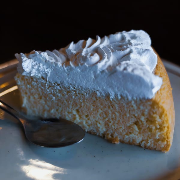 Slice of tres leches cake with whipped cream on a white plate with a spoon.